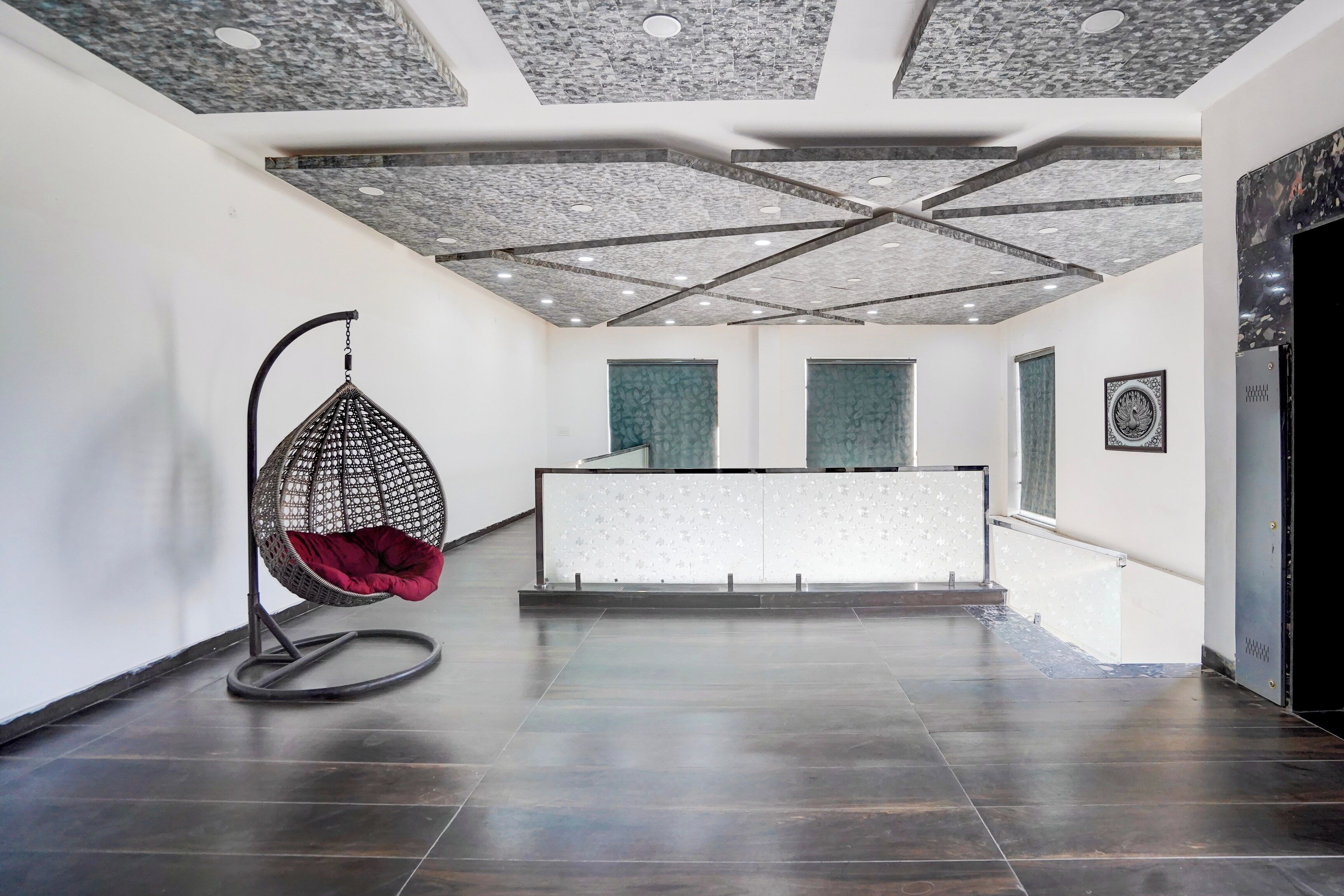 A modern interior with a hanging chair, a reception desk, and a patterned ceiling.