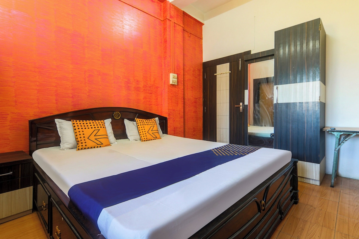 A double bed with a blue bedspread and two pillows, a wooden headboard, and a wooden nightstand.