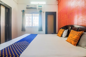A hotel room with a bed, a window with curtains, an air conditioning unit, and a door. - Hotel O Golden Orchid (Jorhat)