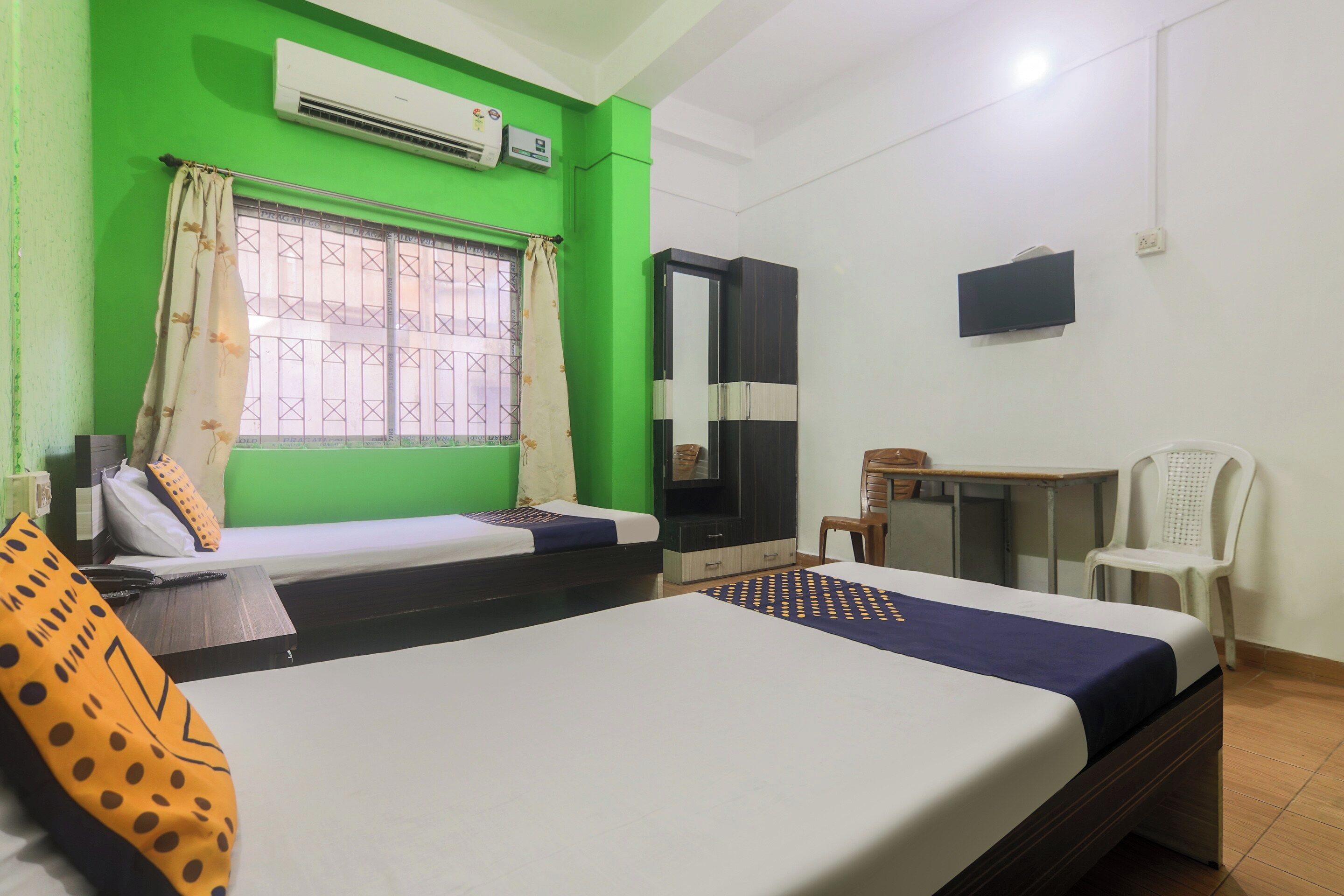 A hotel room with two beds, a desk, a chair, a TV, and an air conditioning unit.
