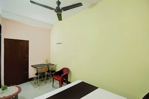 A room with a ceiling fan, a table with chairs, a door, and a small potted plant. - Hotel O RB Atithisala (Jorhat)
