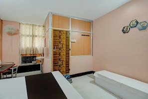 A room with a bed, a desk, a chair, a fan, and a window with a curtain. - Hotel O RB Atithisala (Jorhat)