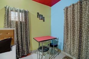 A small room with a bed, a table, and a chair. There are curtains on the windows. - Hotel O RB Atithisala (Jorhat)
