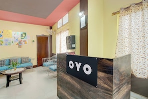 A reception area with a reception desk labeled 'OYO,' a blue sofa, a small table with a plant, and a wall with various artworks. - Hotel O RB Atithisala (Jorhat)