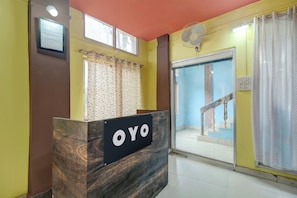 A reception desk with a sign reading 'OYO' in a hotel lobby with a staircase and a fan.
