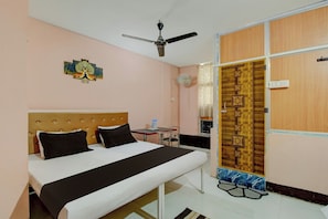 A hotel room with a bed, a ceiling fan, a wall-mounted artwork, and a wooden door with decorative panels. - Hotel O RB Atithisala (Jorhat)