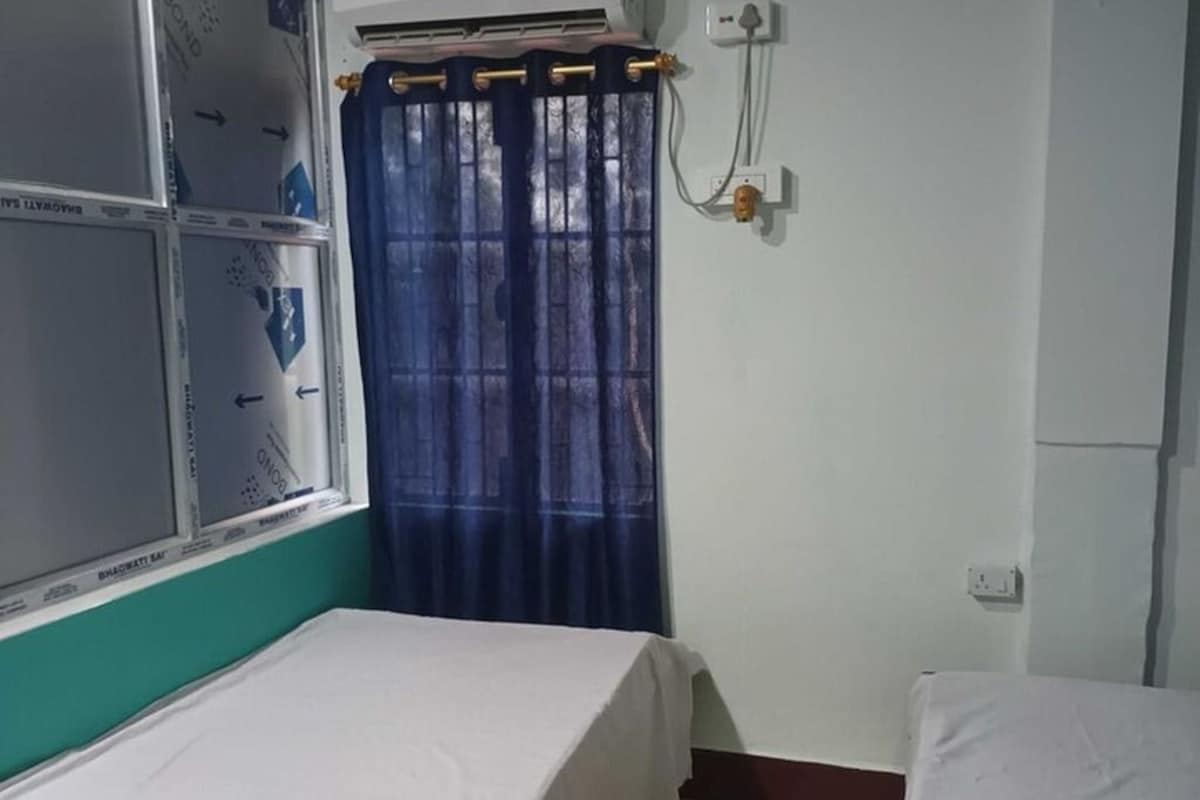 A room with two beds, a window with a curtain, and an air conditioning unit.