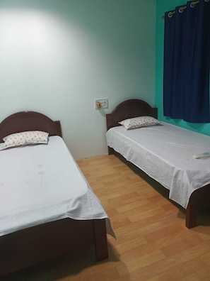 A room with two single beds, a wooden floor, a light switch on the wall, and a blue curtain on the window. - Hotel O CHANDRAWALI LODGE (Jorhat)