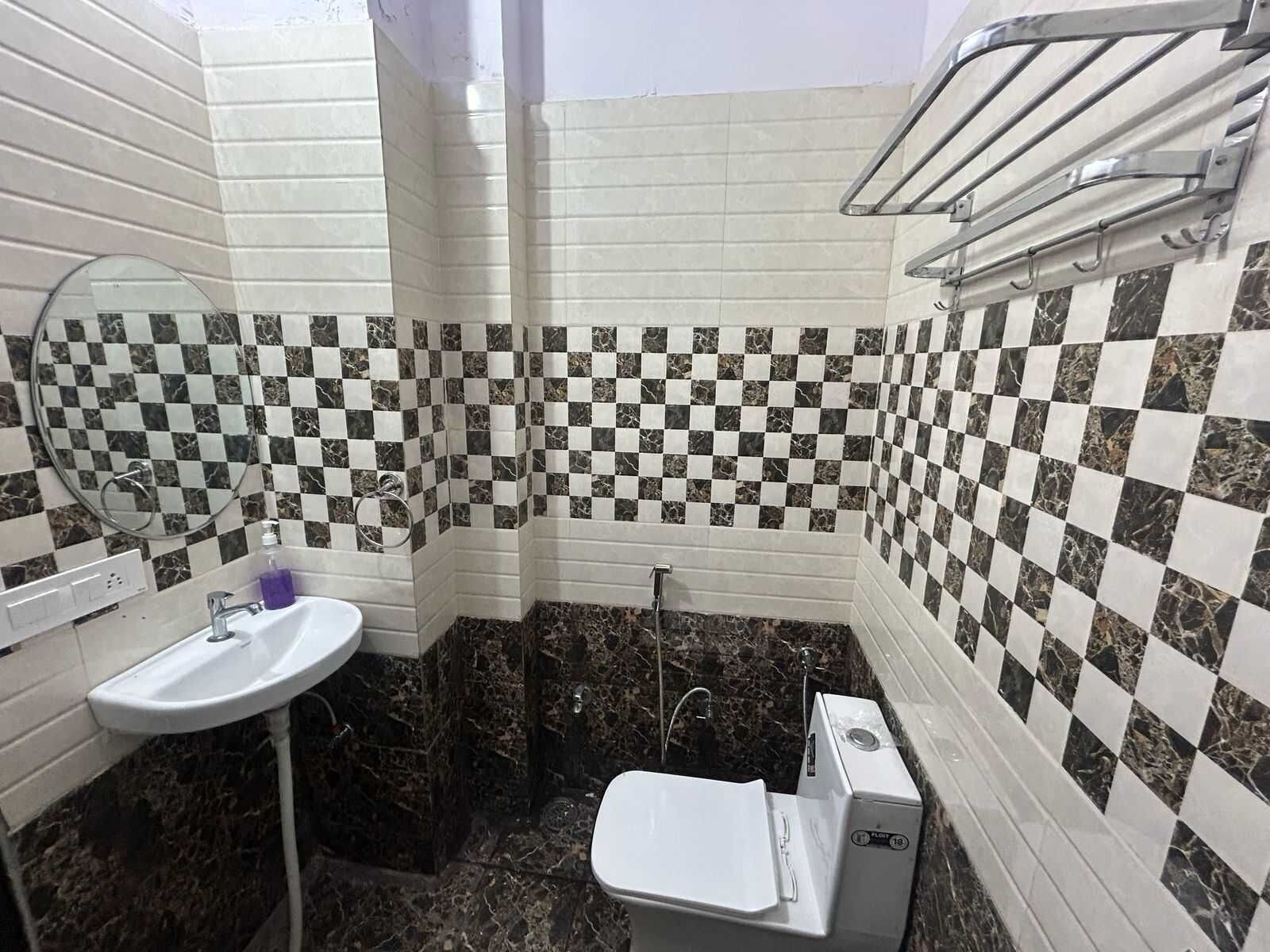 A bathroom with a checkered tile wall, a white sink, a mirror, and a toilet.
