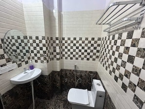 A bathroom with a checkered tile wall, a white sink, a mirror, and a toilet. - Collection O Rampura Rawat Resort (Tivari)