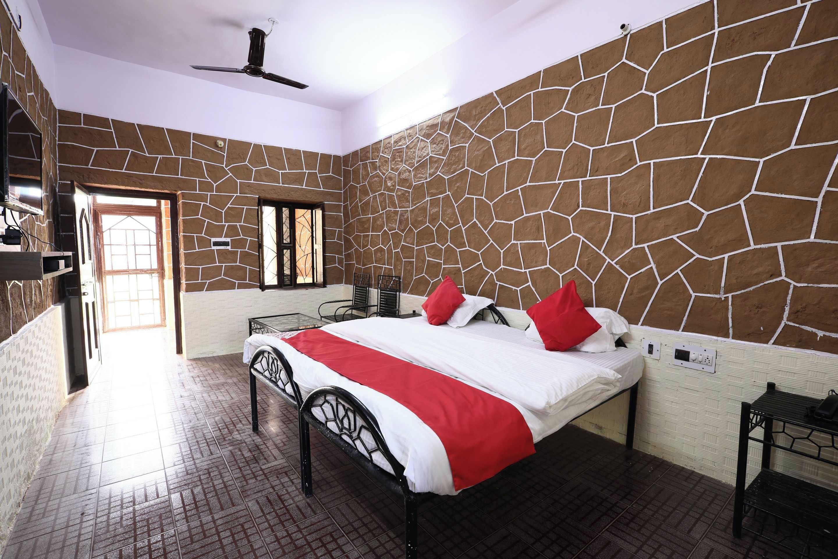A bedroom with a stone-patterned wall, a bed with a red and white bedspread, and a ceiling fan.