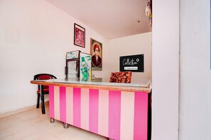 A reception desk with a striped pink and white design, a framed portrait on the wall, and a sign indicating a company-serviced collection. - Collection O Rampura Rawat Resort (Jodhpur)