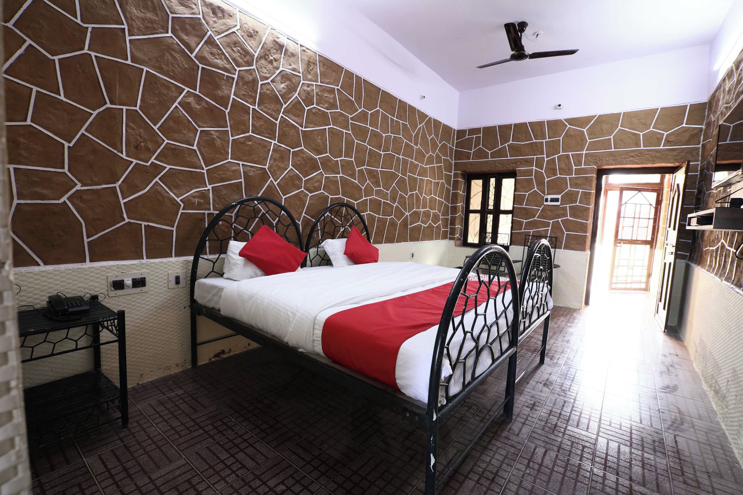 A room with a stone-patterned wall, a bed with a metal frame, a ceiling fan, and a door leading to another room.
