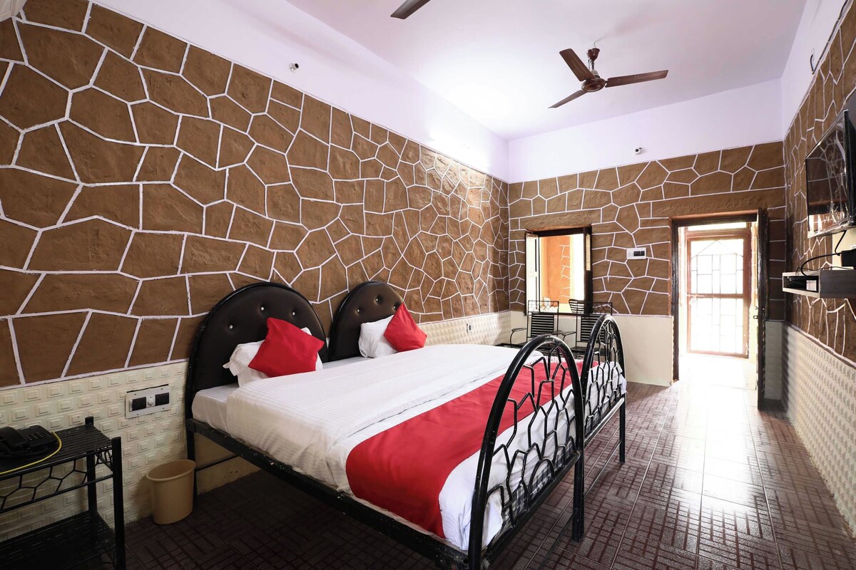 A bedroom with a stone-patterned wall, a bed with a red and white bedspread, a ceiling fan, and a door leading to another room.