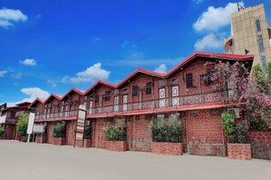 A multi-story building with a distinctive red and brown patterned facade, balconies with intricate railings, and a clear blue sky in the background. - Collection O Rampura Rawat Resort (Tivari)