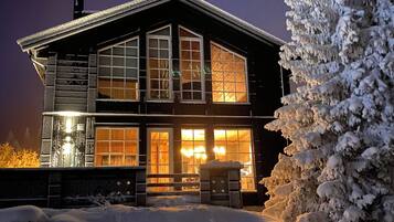 A two-story building with large windows and a visible door, surrounded by snow-covered ground and a snow-covered tree.