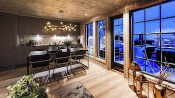 A modern kitchen with wooden cabinets, a dining area with a table and chairs, and large windows with a view of a snowy landscape.