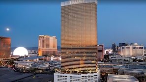 Un edificio de gran altura con la palabra 'TRUMP' escrita en la parte superior, rodeado de otros edificios y una gran cúpula iluminada al fondo.