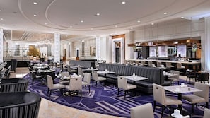 Un amplio hall de hotel con varias zonas de estar, un bar y una recepción.