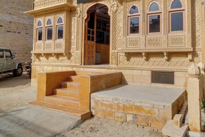 Un bâtiment doté de détails architecturaux élaborés, un escalier menant à l’entrée et un véhicule garé à l’extérieur.