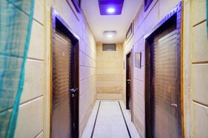 Un couloir avec des portes fermées, un sol carrelé et un luminaire au plafond.