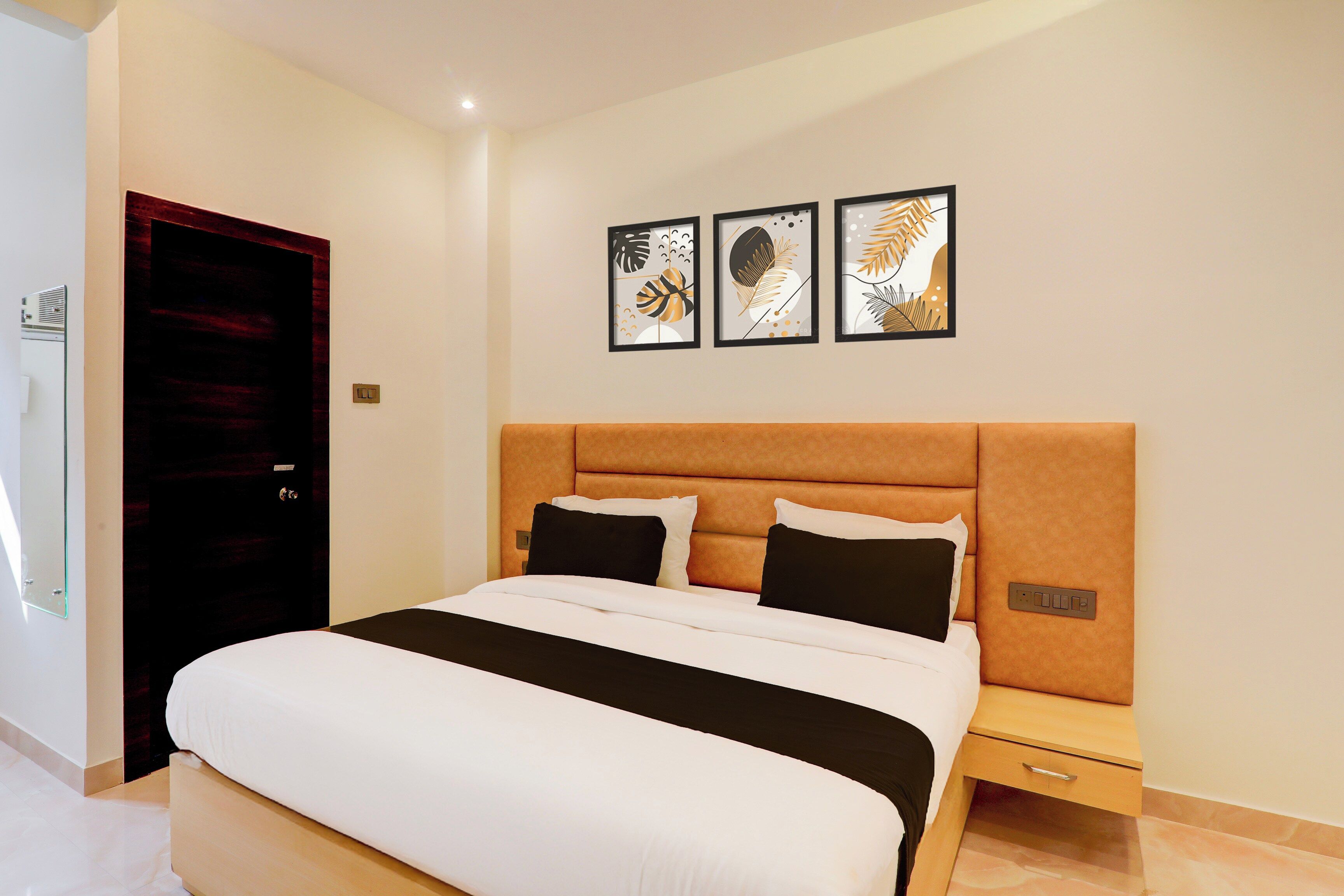 A hotel room with a bed, a nightstand, a wall-mounted power outlet, and a door.