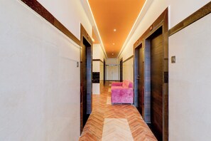 Un pasillo de hotel con piso de diseño espiga, un sofá rosa y un espejo en la pared.