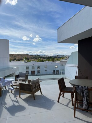 Terraço no telhado com conjunto de jantar, cadeiras e vista de edifícios ao longe.