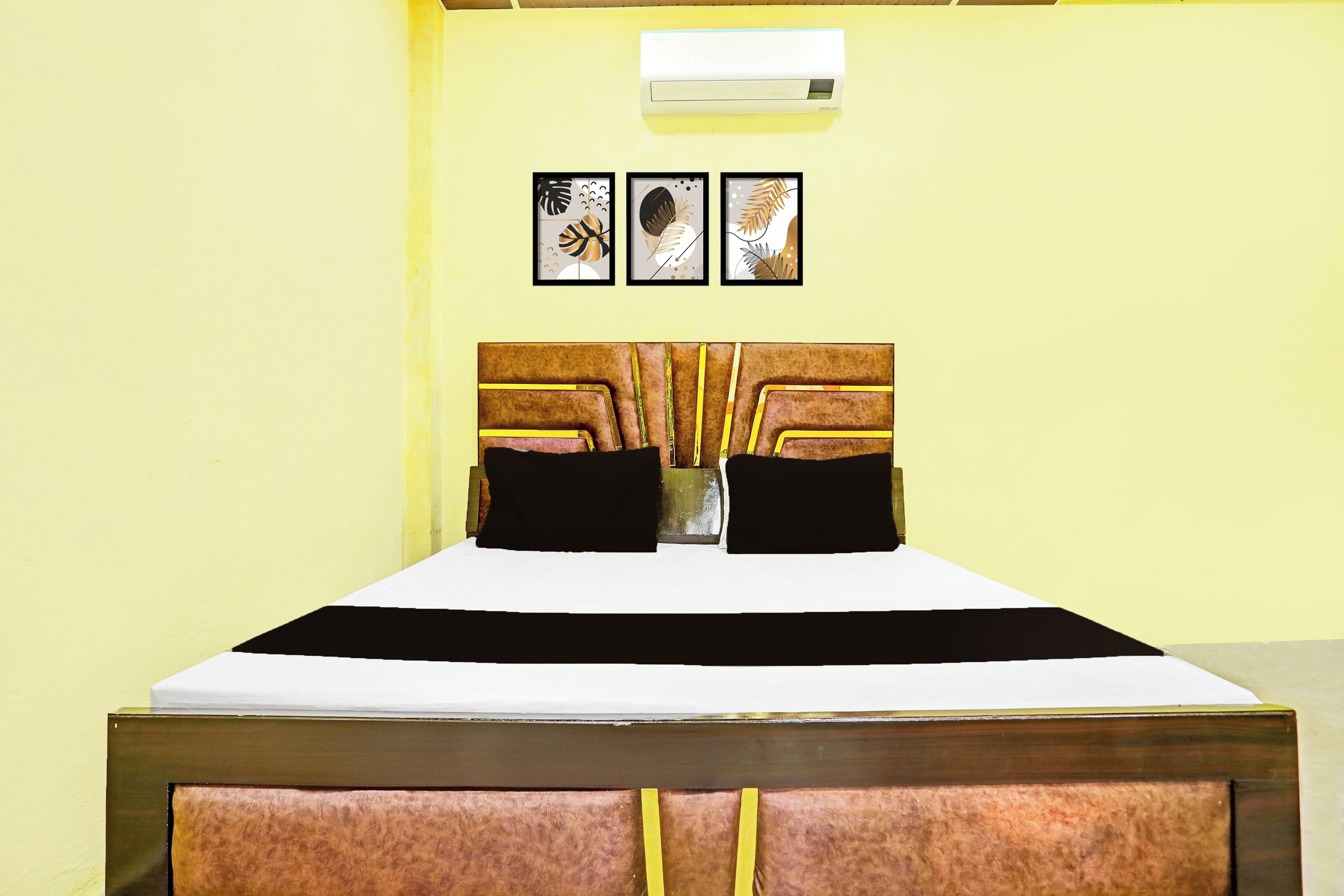A bed with a wooden headboard and two black pillows, a white bedspread, and three framed wall art pieces above it.