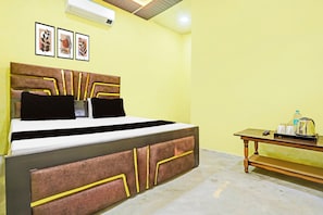 Ein Zimmer mit einem Bett, einem Nachttisch mit Wasserkocher und gerahmten Kunstwerken an der Wand.