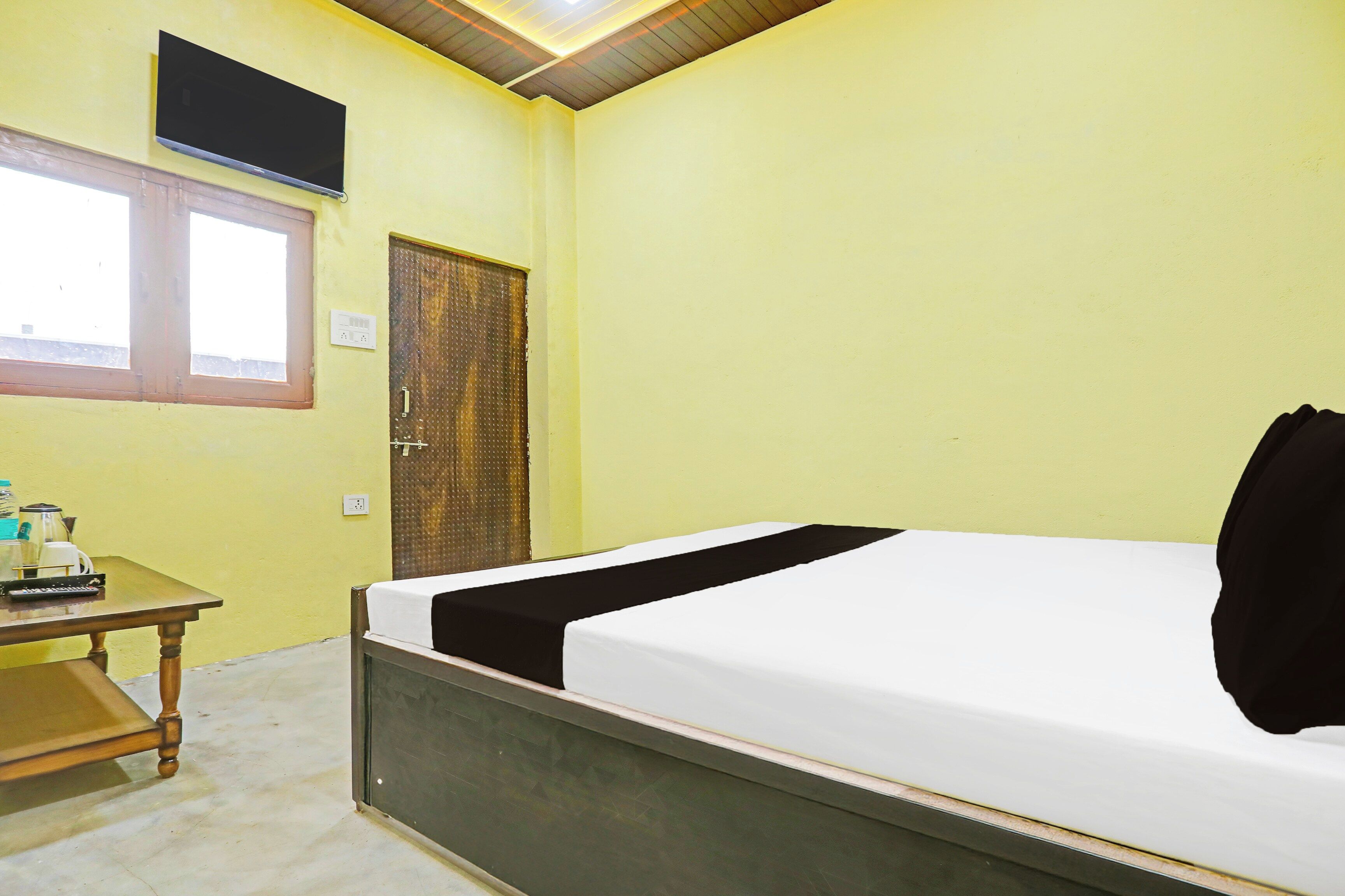 A room with a bed, a table with a kettle, a window, and a door.