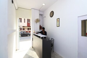 Un área de recepción con un mostrador, sillas, un ventilador, un reloj y un cuadro en la pared.