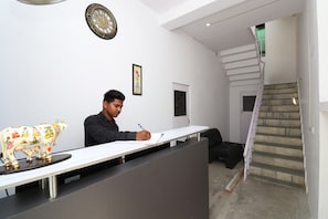 A man writing at a desk in a room with a staircase and a door. - Hotel O Krishna Inn (Lucknow)