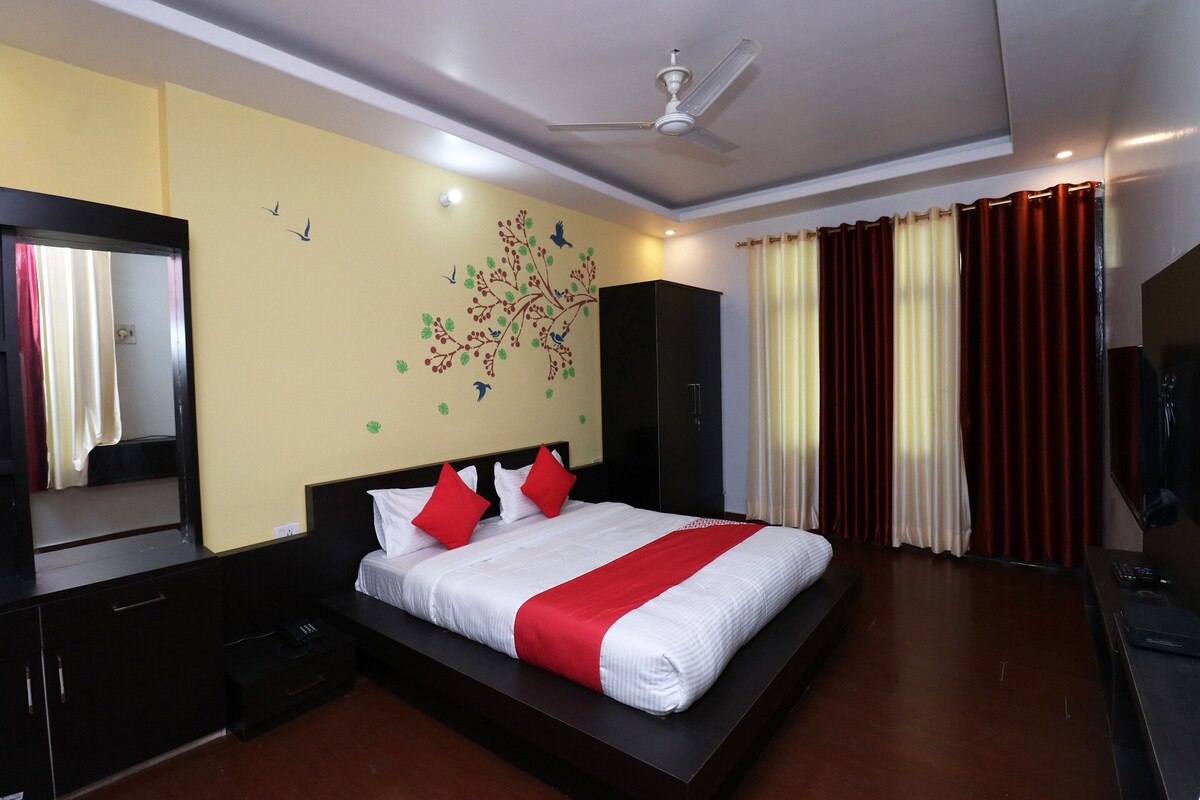 A hotel room with a bed, a wardrobe, a mirror, a ceiling fan, and a window with curtains.