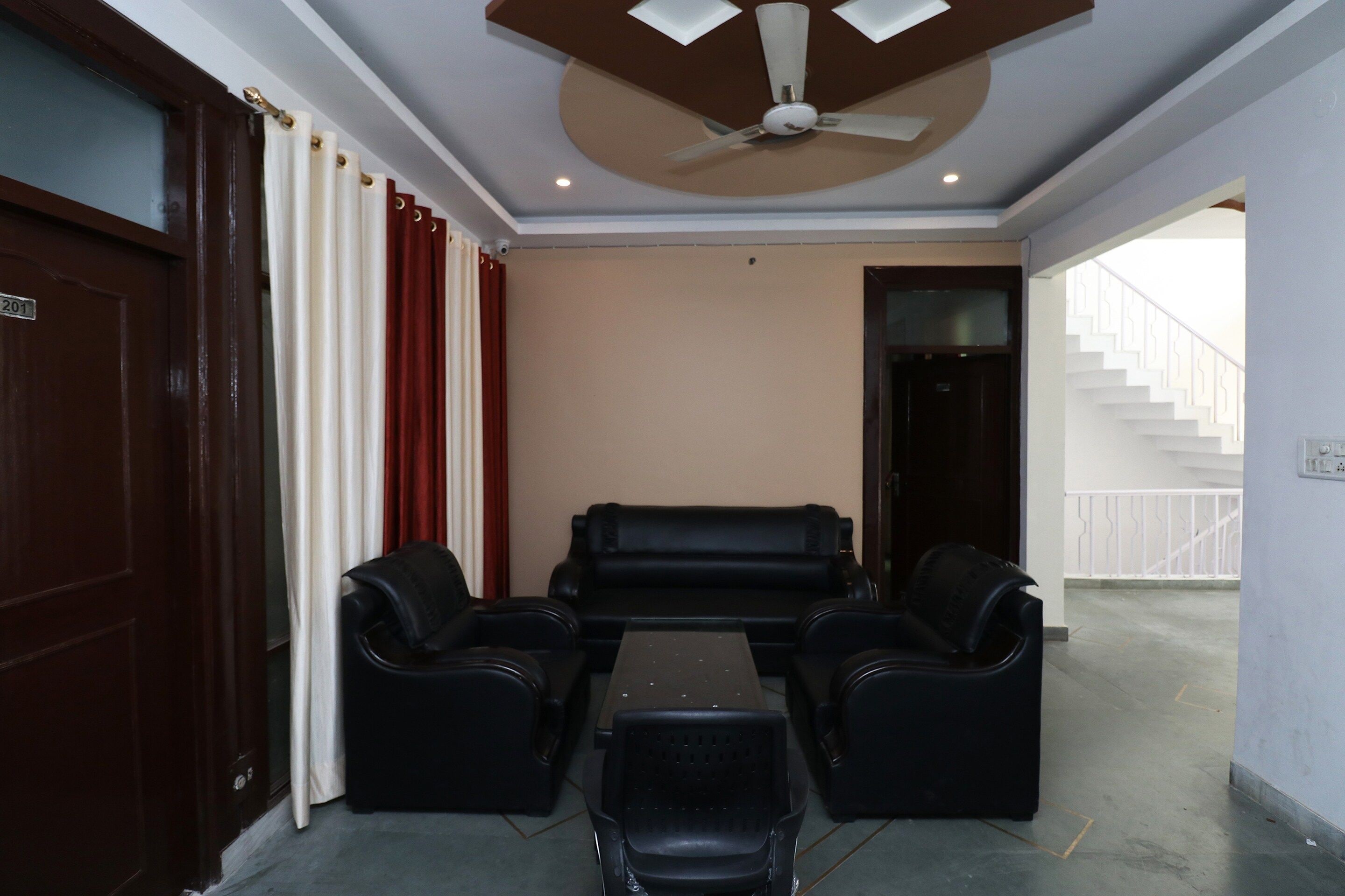 A room with a ceiling fan, a black leather sofa, a small table, and a door with a number plate.