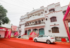 A white multi-story building with balconies and a car parked in front. - Hotel O Jc Guest House (Lucknow)