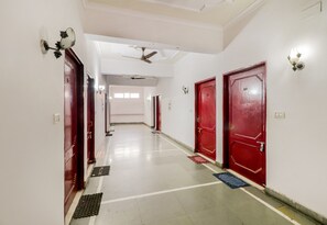 A hotel corridor with multiple red doors, a ceiling fan, and a light fixture on the wall. - Hotel O Jc Guest House (Lucknow)