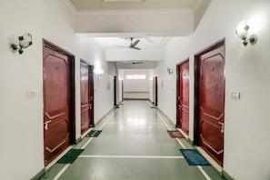 A hotel corridor with red doors, a ceiling fan, and a light fixture on the wall. - Hotel O Jc Guest House (Lucknow)