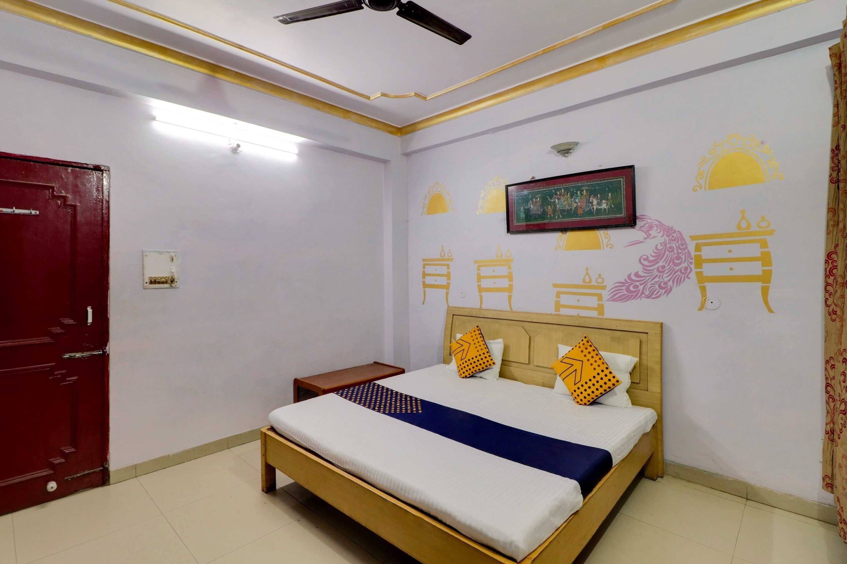 Habitación de hotel con una cama individual, ventilador de techo, puerta roja y decoración mural.