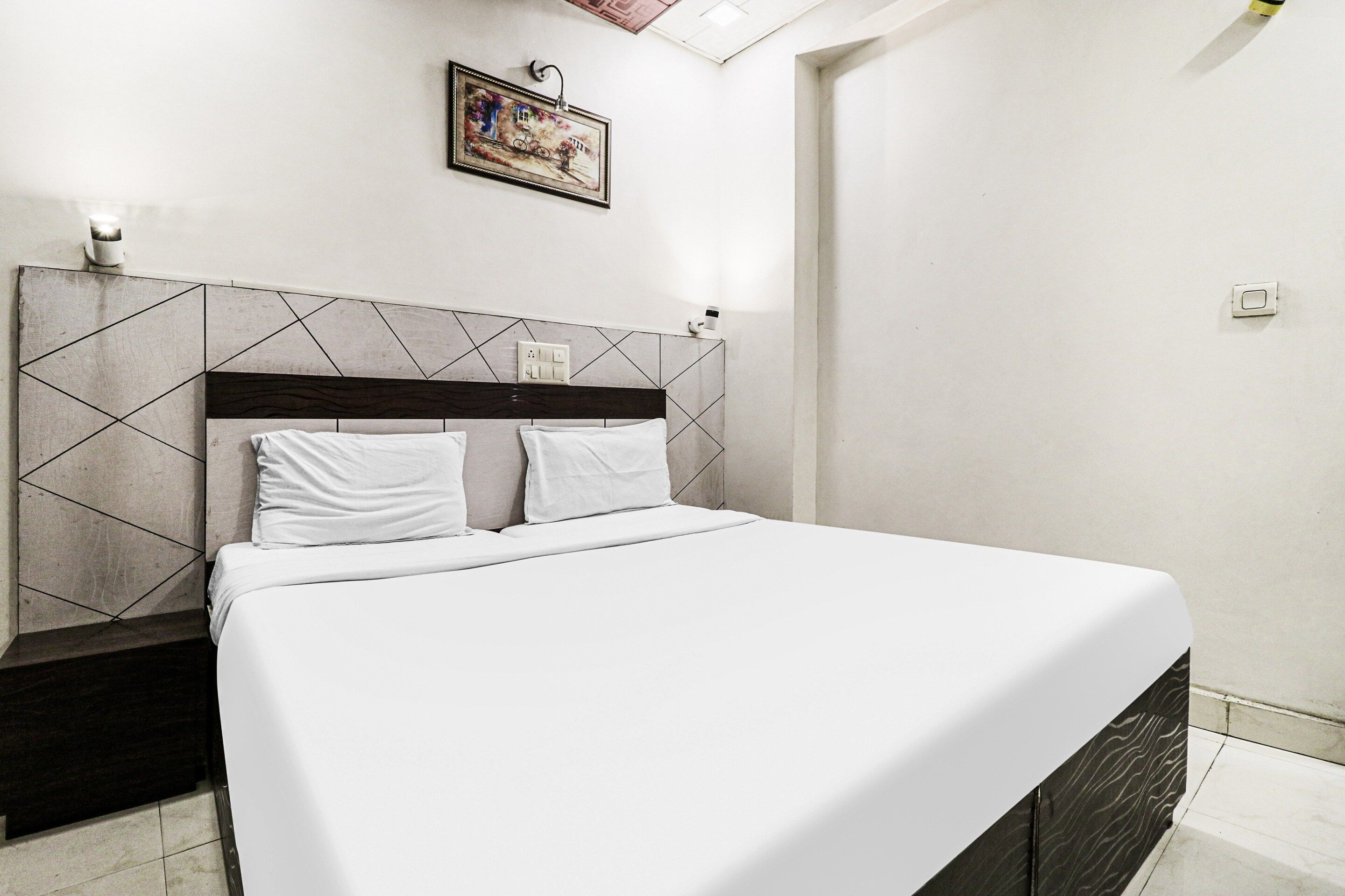 Una cama con ropa blanca en una habitación con cabecera de estampado geométrico y una lámpara de pared.