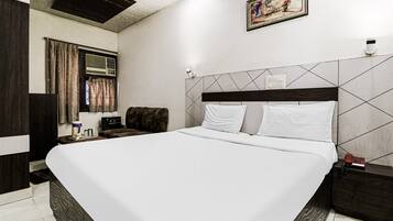 A hotel room with a large bed, a headboard with a geometric pattern, a bedside table with a lamp, and a painting on the wall.
