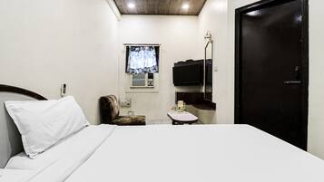 Quarto de hotel com cama, uma cadeira, mesa pequena, televisão e porta.
