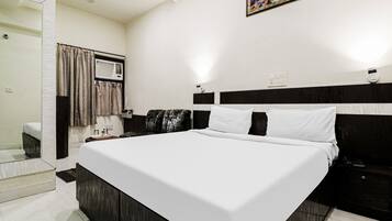 A hotel room with a large bed, a bedside table, a chair, a window with curtains, and a wall-mounted air conditioning unit.