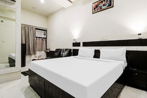 A hotel room with a large bed, a bedside table, a chair, a window with curtains, and a wall-mounted air conditioning unit. - Hotel O by OYO Surya (Ludhiana)