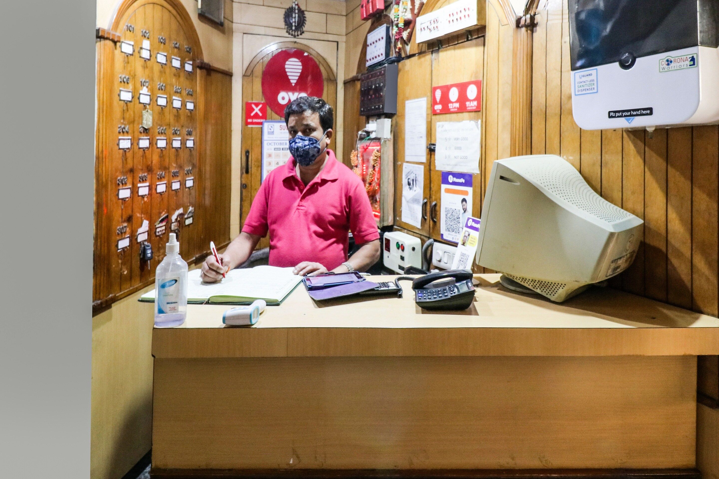 Un hombre en la recepción, con una computadora, un teléfono y varios documentos.