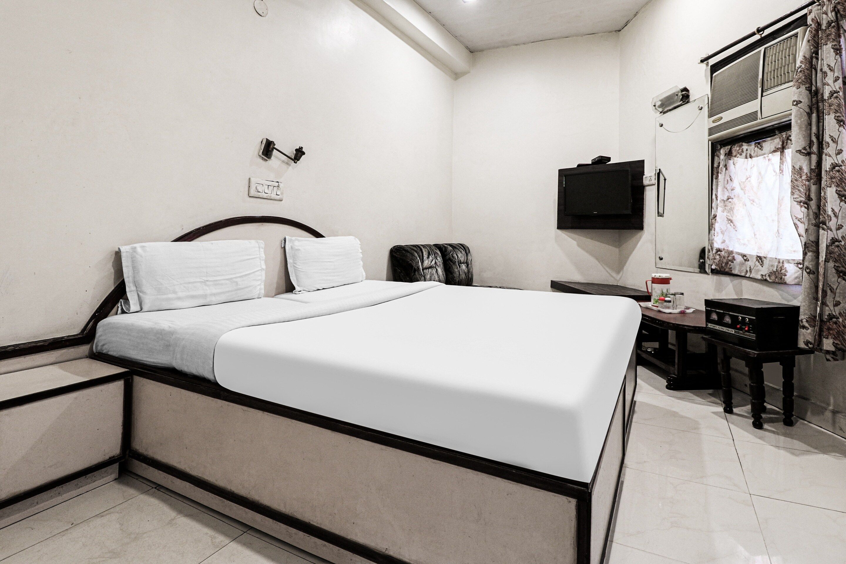 Un dormitorio con cama, mesitas de noche, televisor y ventana con cortinas.