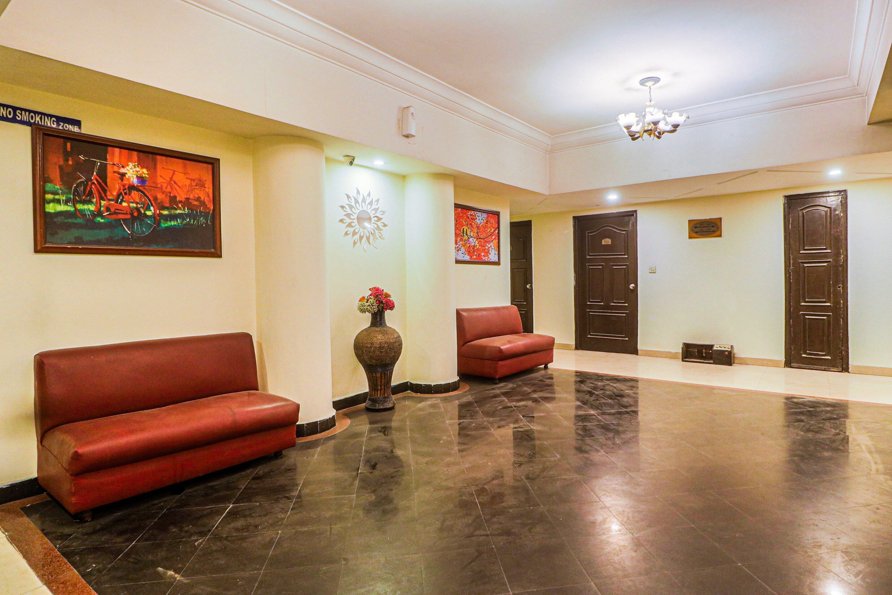 Um lobby com um sofá vermelho, um vaso com flores e um quadro na parede.
