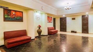 Um lobby com um sofá vermelho, um vaso com flores e um quadro na parede.