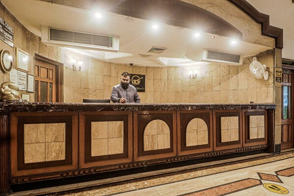 A reception desk with a man standing behind it, a clock, and a sign that reads 'Welcome'.