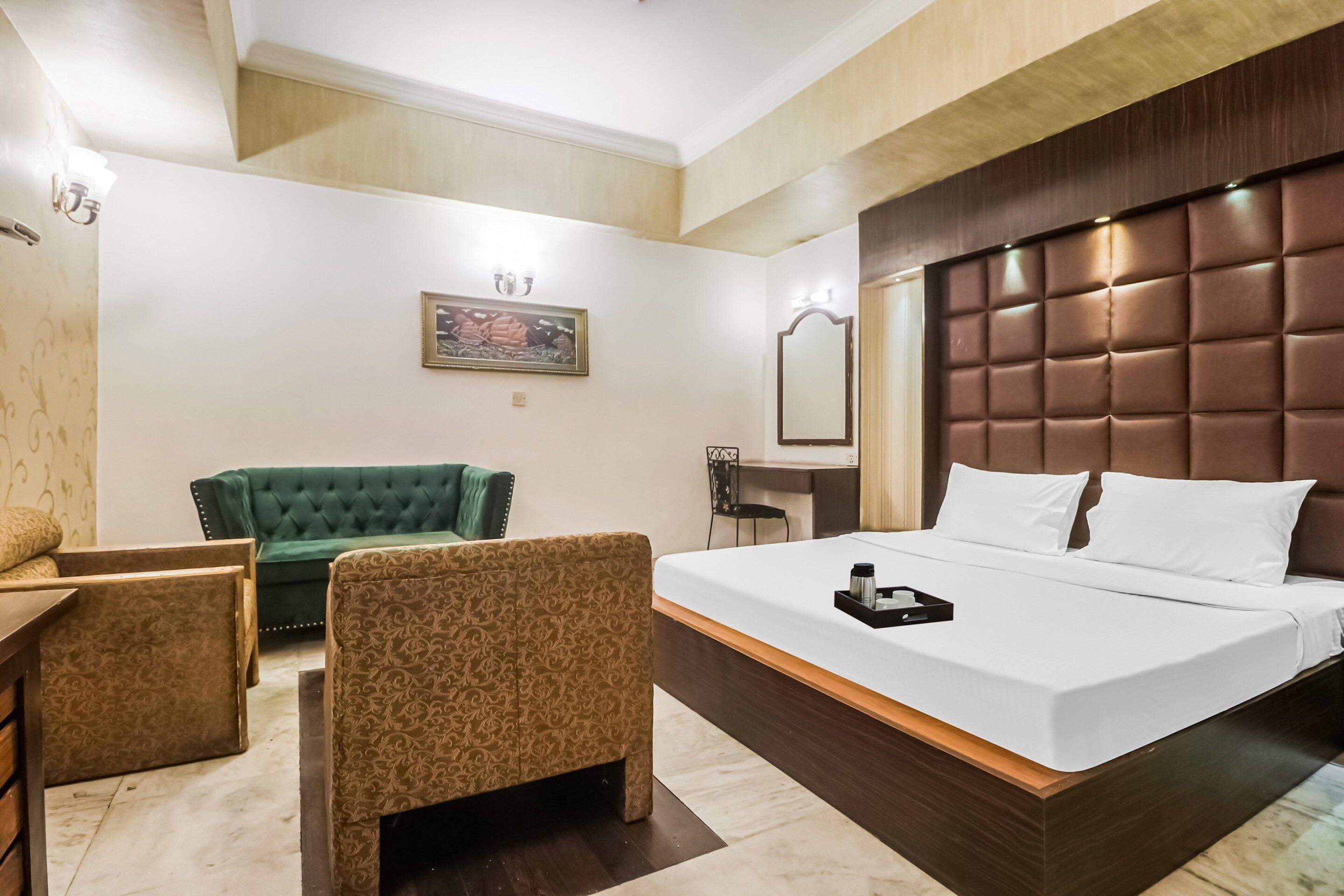 A hotel room with a large bed, a green sofa, a small table, and a mirror.